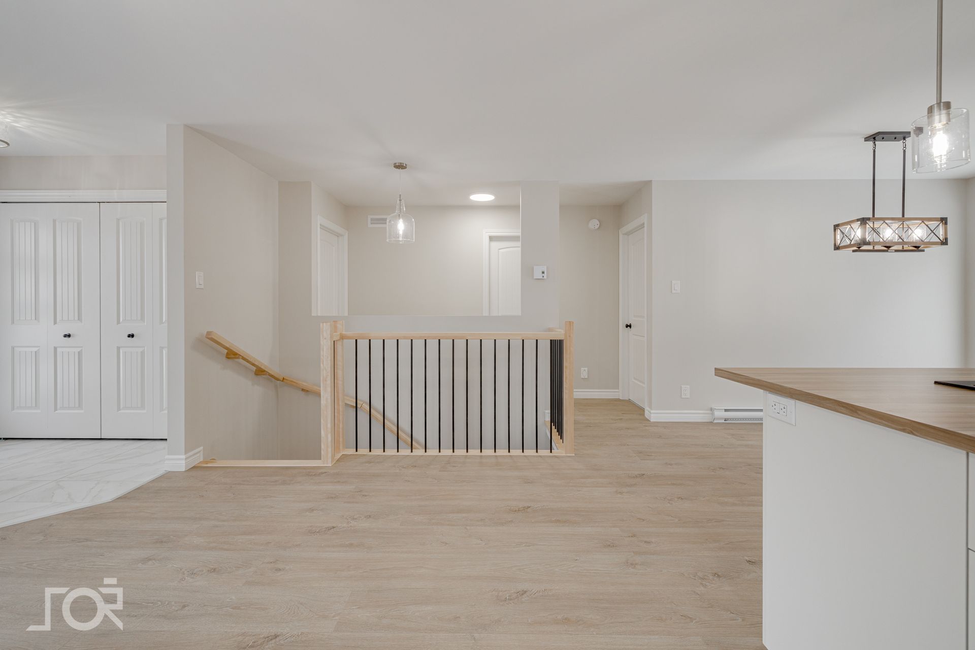 Espace de vie à aire ouverte avec murs neutres, escalier et parquet clair.