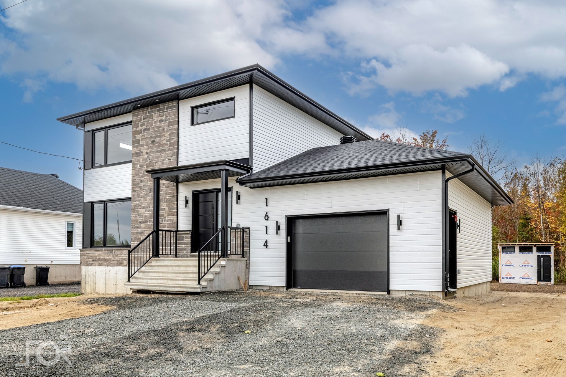 Une grande maison blanche avec une porte de garage noire est à vendre.