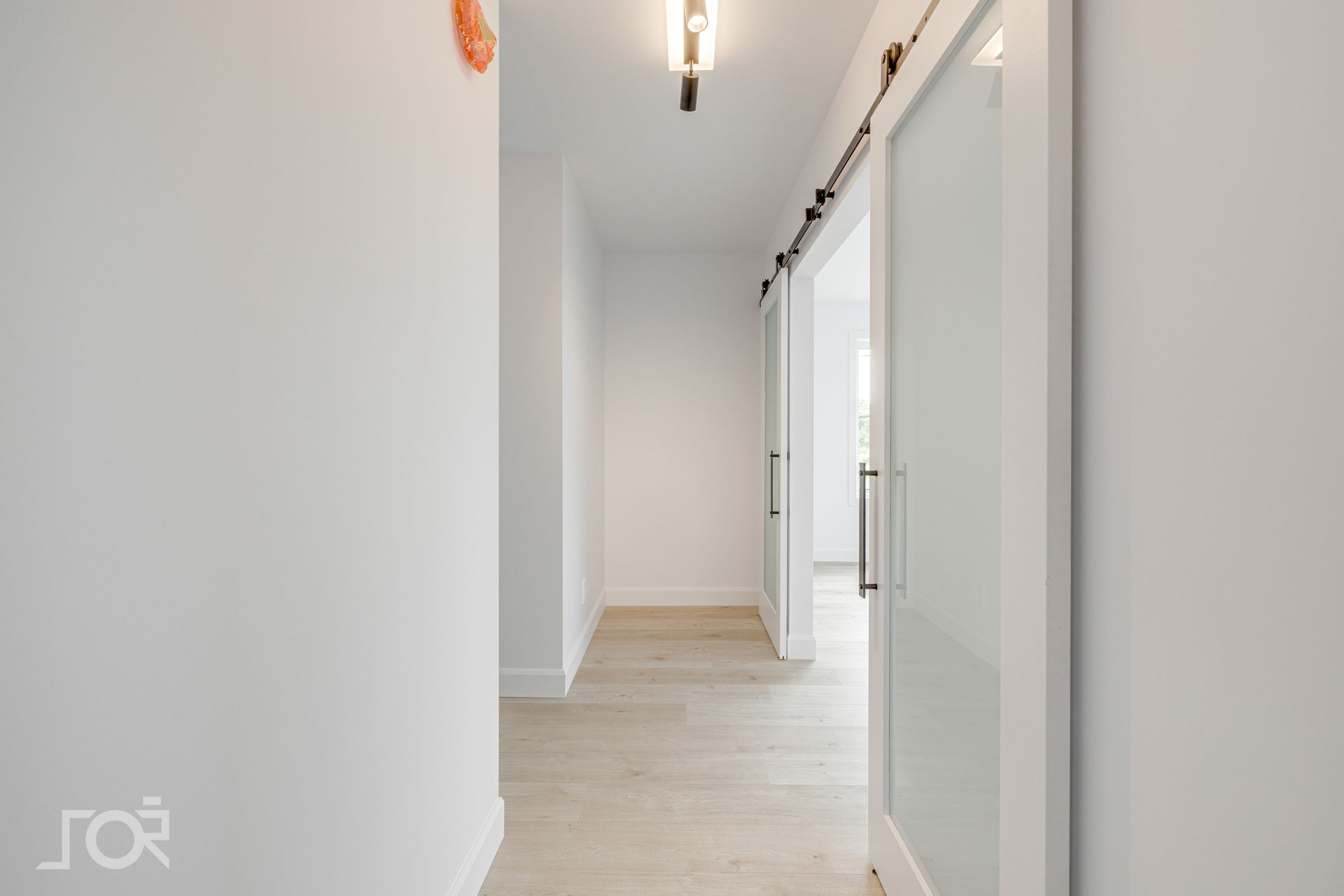 Un couloir vide avec une porte coulissante en verre et des murs blancs.