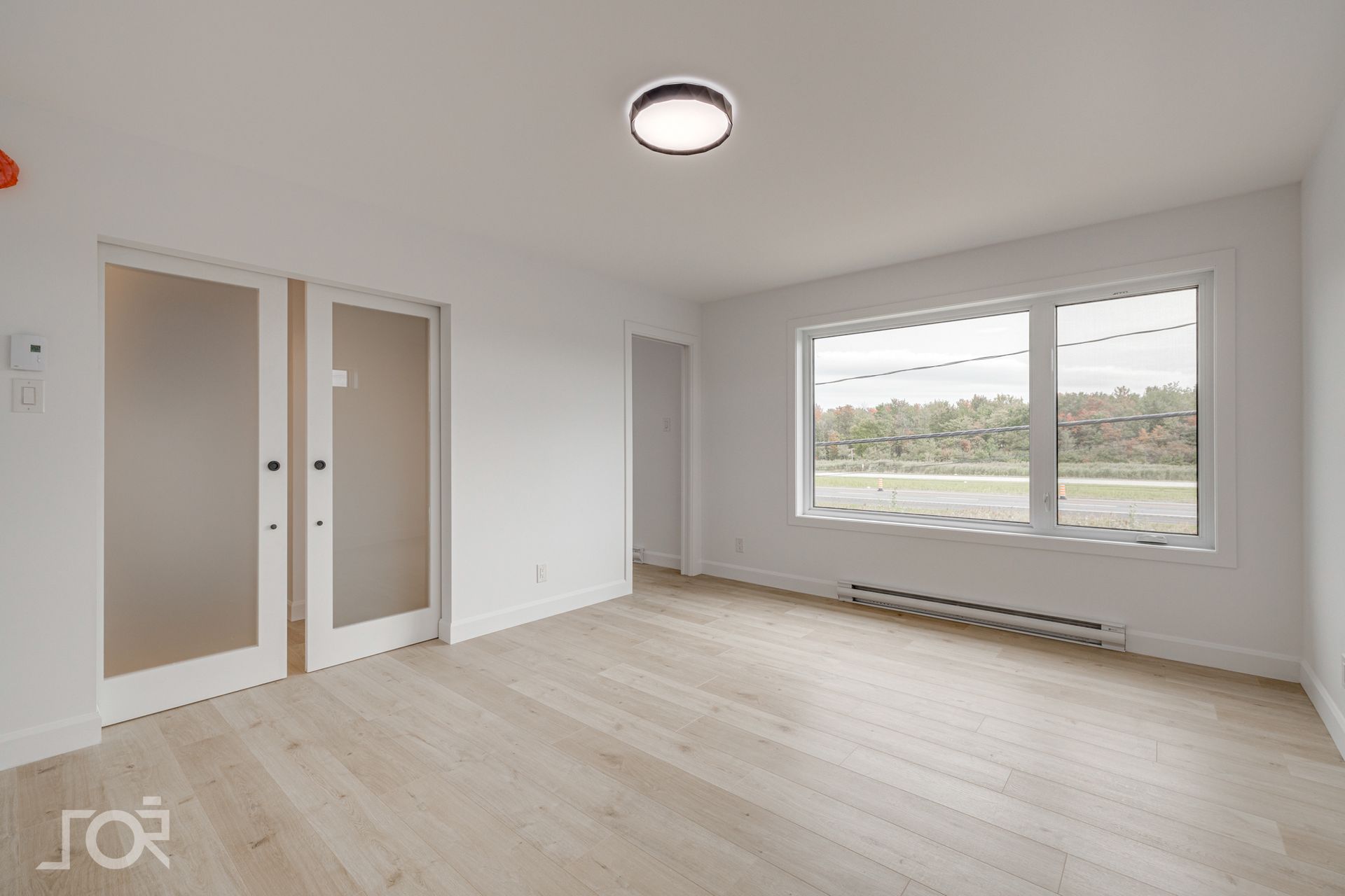 Un salon vide avec parquet et deux fenêtres.