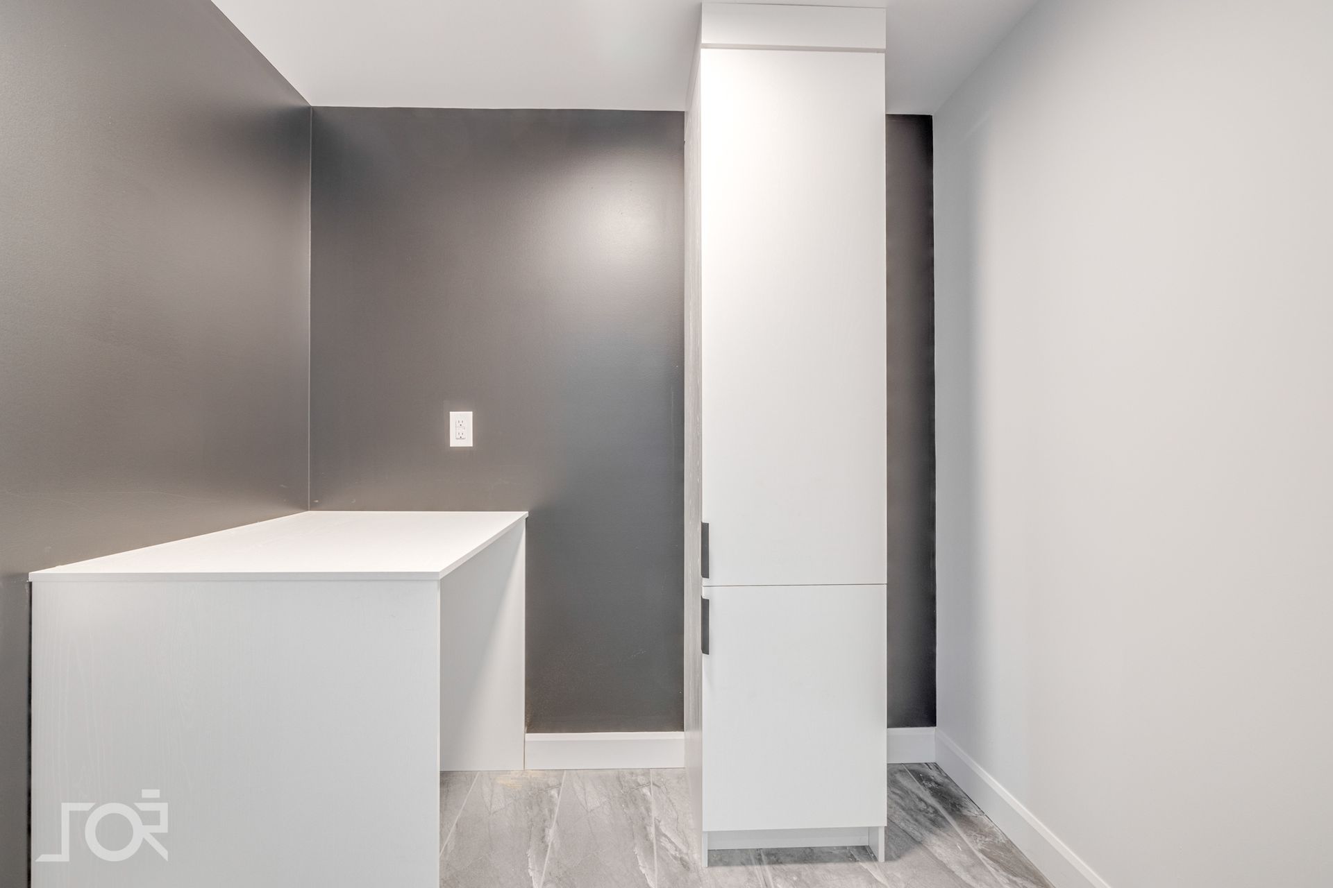 Une buanderie avec un mur gris et des armoires blanches