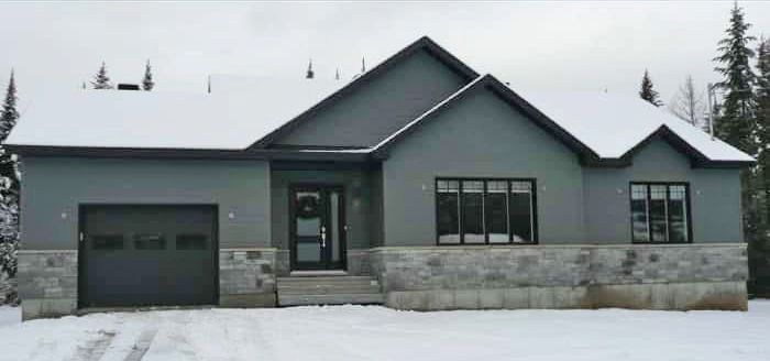 Une maison grise avec une porte de garage noire est recouverte de neige.
