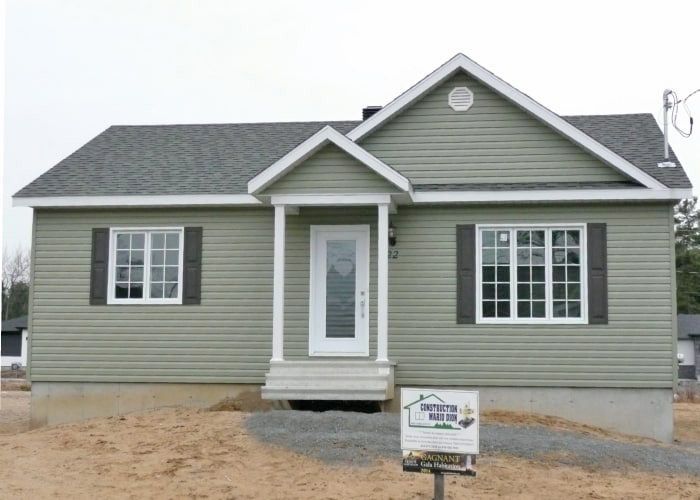 Une petite maison verte avec un panneau devant