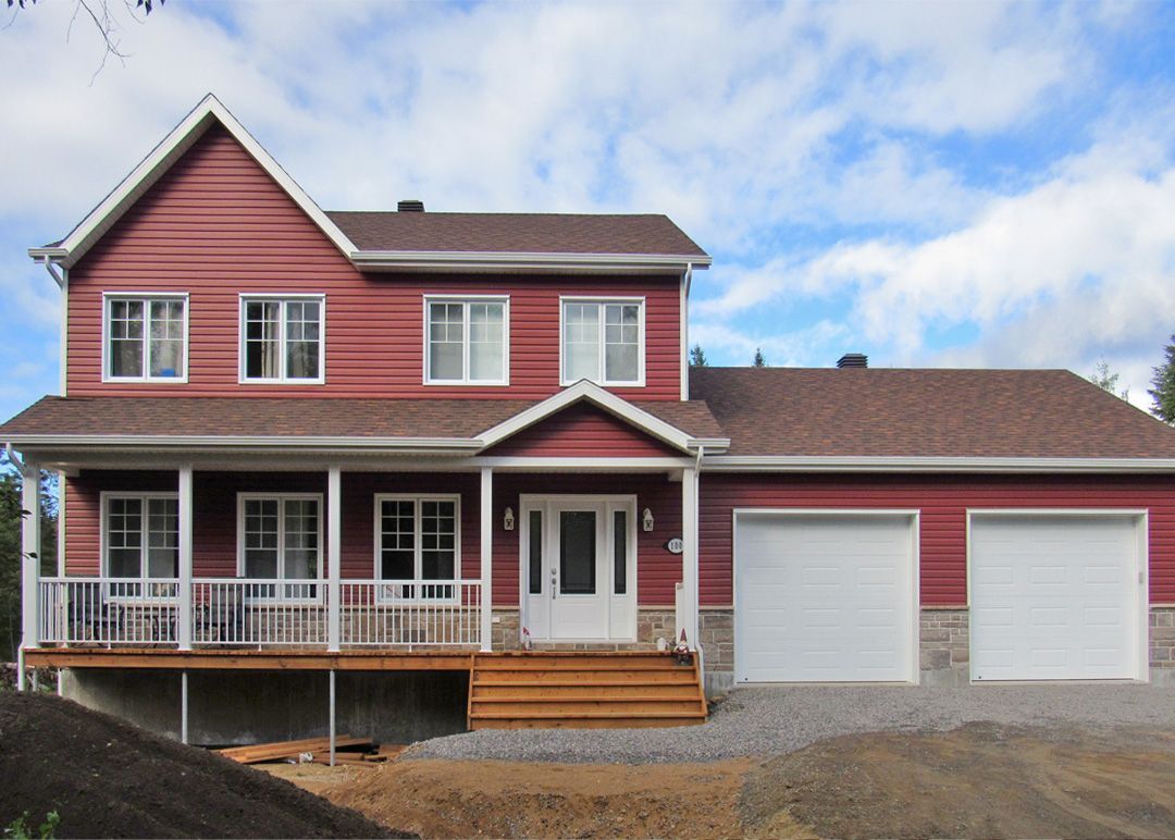 Une grande maison rouge avec des portes de garage blanches et un porche