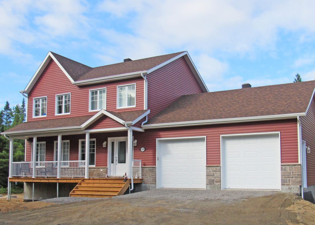 Une grande maison rouge avec deux portes de garage et un porche