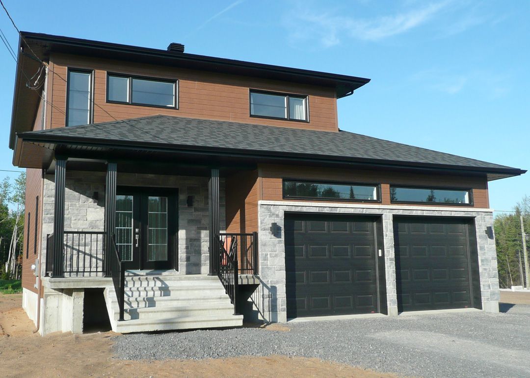 Une grande maison en briques avec deux portes de garage noires