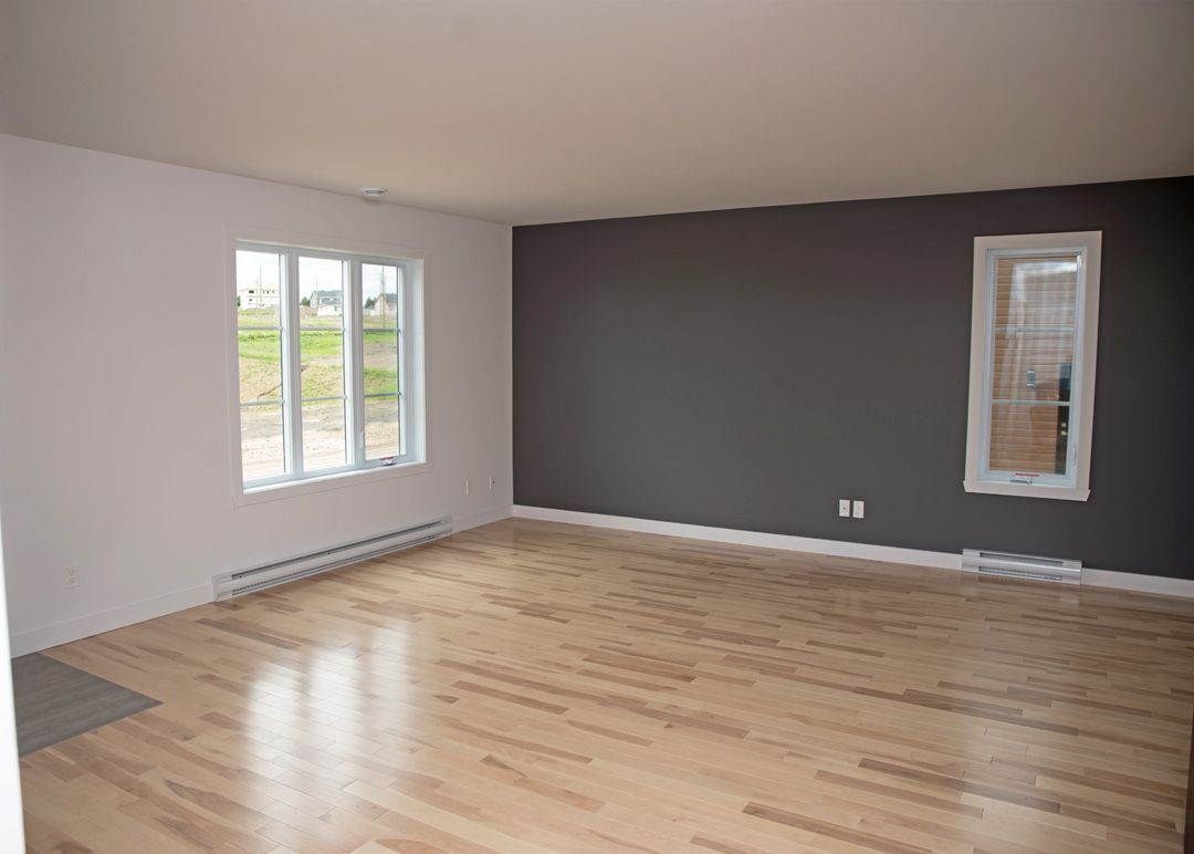 Un salon vide avec du parquet et des murs gris.