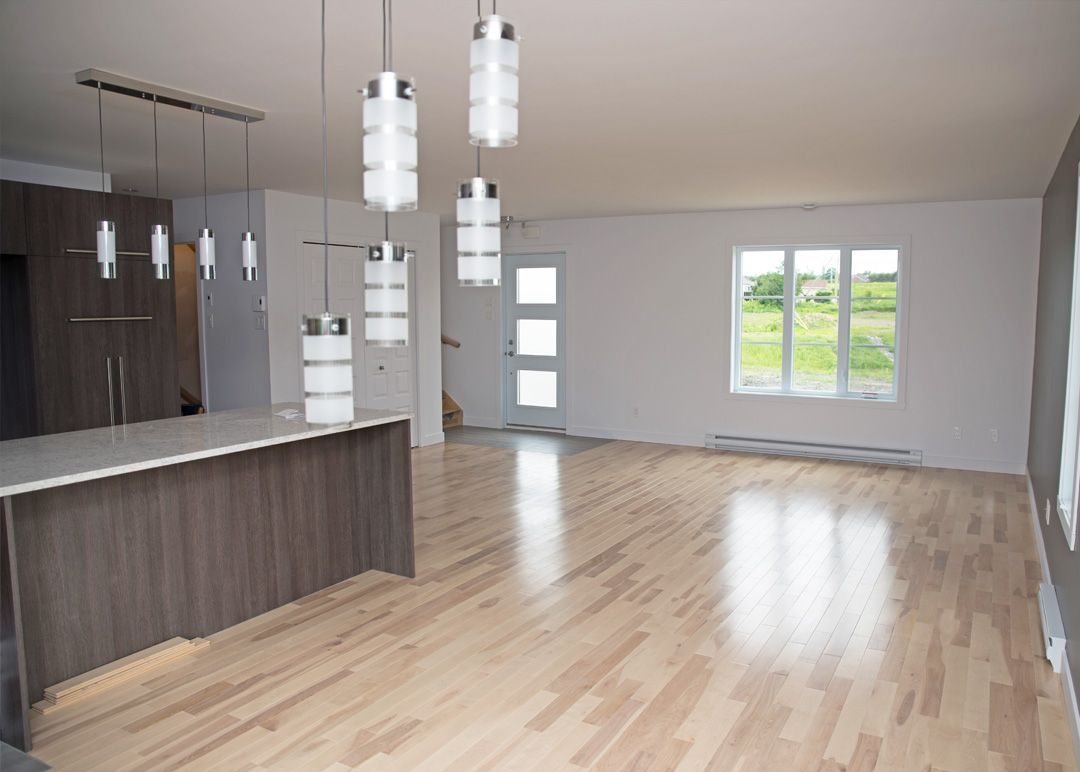 Un salon vide avec parquet et une cuisine.