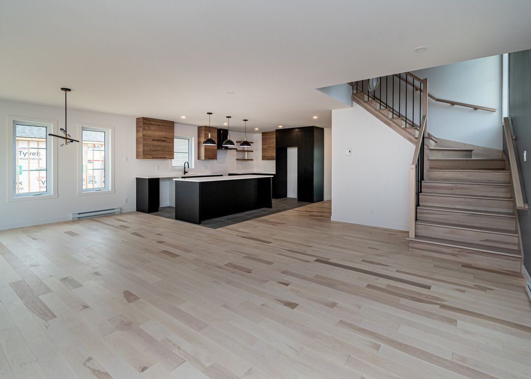 Un salon vide avec parquet et escalier menant à une cuisine.