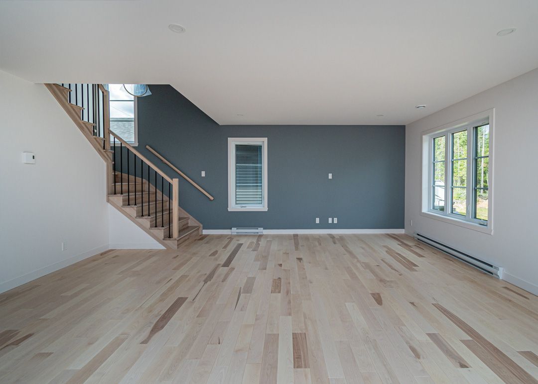 Un salon vide avec parquet et escaliers.