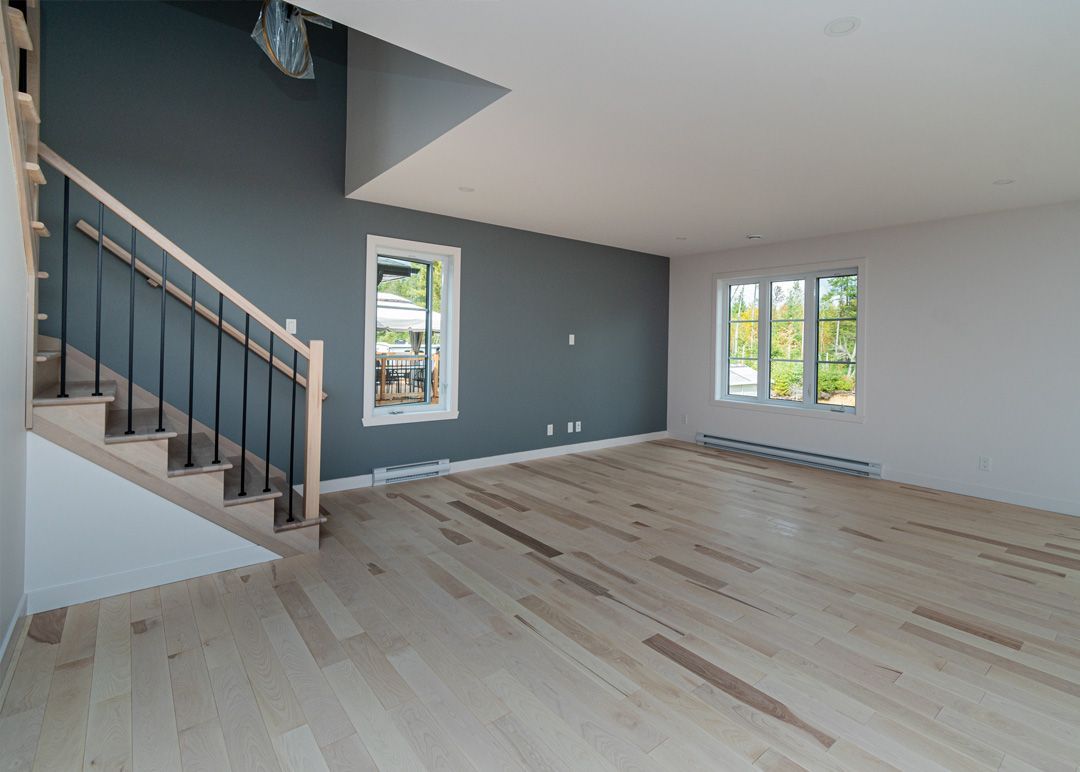 Un salon vide avec parquet et escaliers.