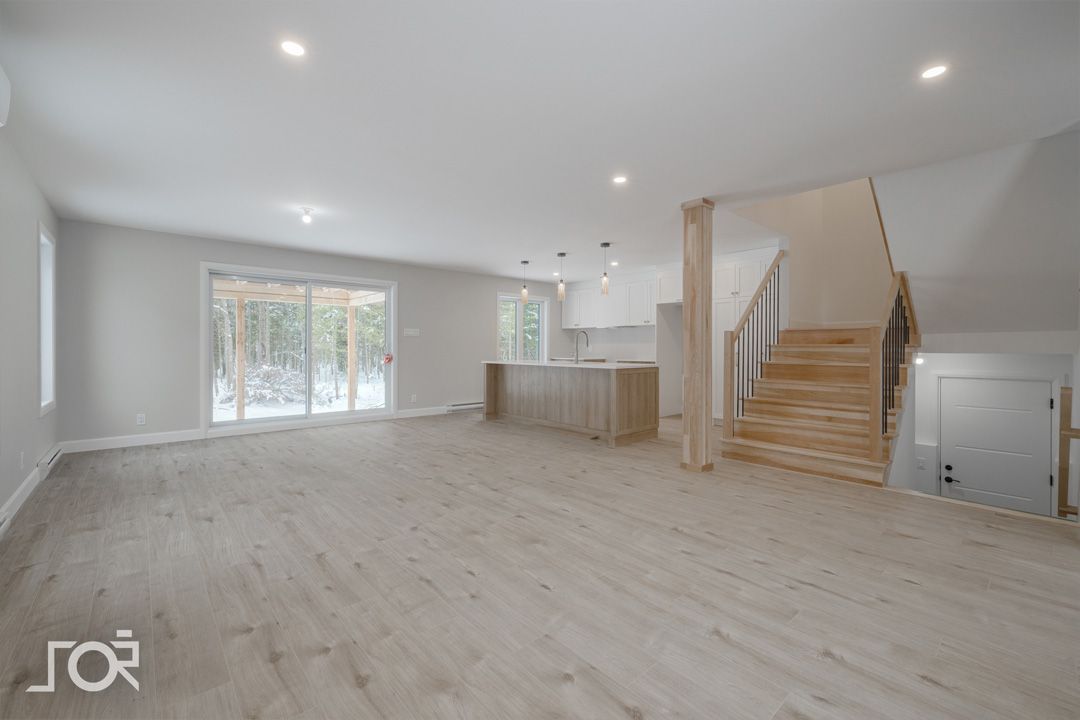 Un salon vide avec du parquet et des escaliers dans une maison.