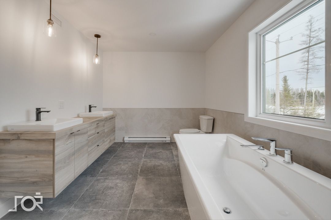 Une salle de bain avec baignoire, lavabos, toilettes et fenêtre.