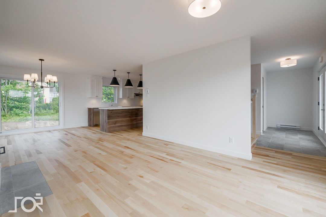 Un salon vide avec du parquet et des murs blancs.