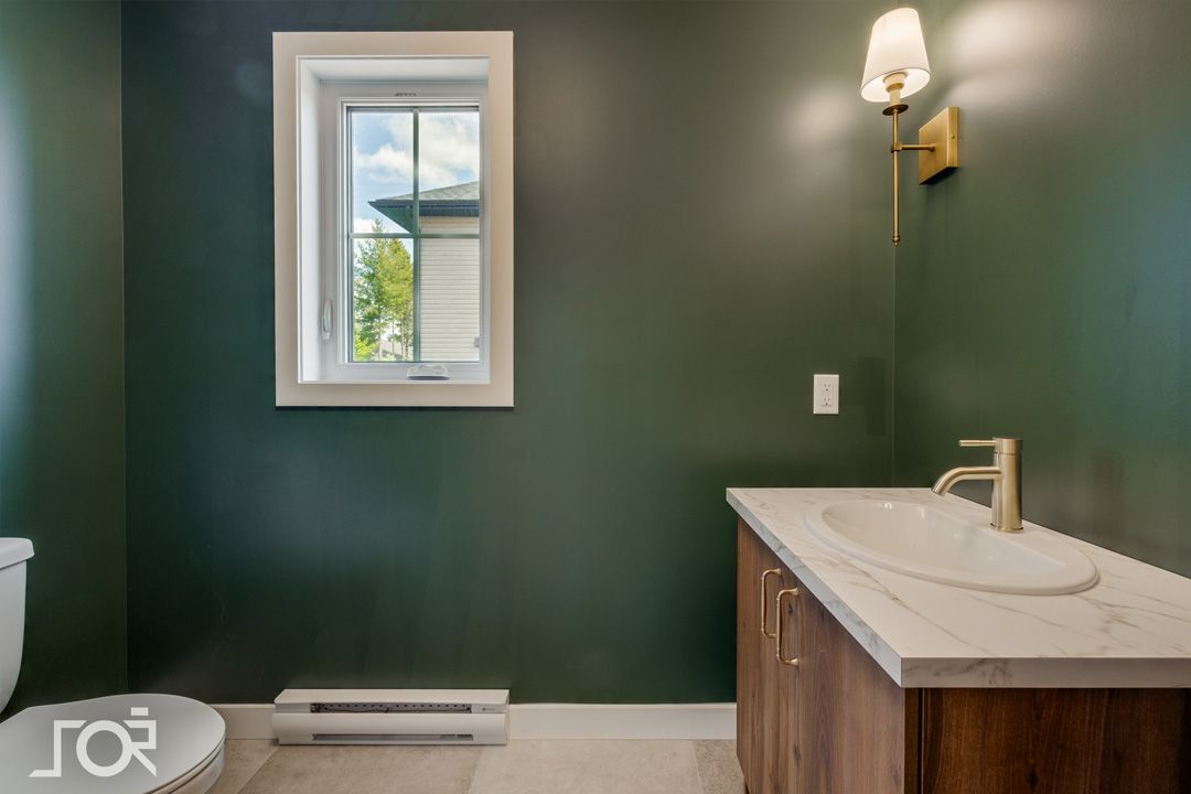 Une salle de bain avec des murs verts, un lavabo, un WC et une fenêtre.