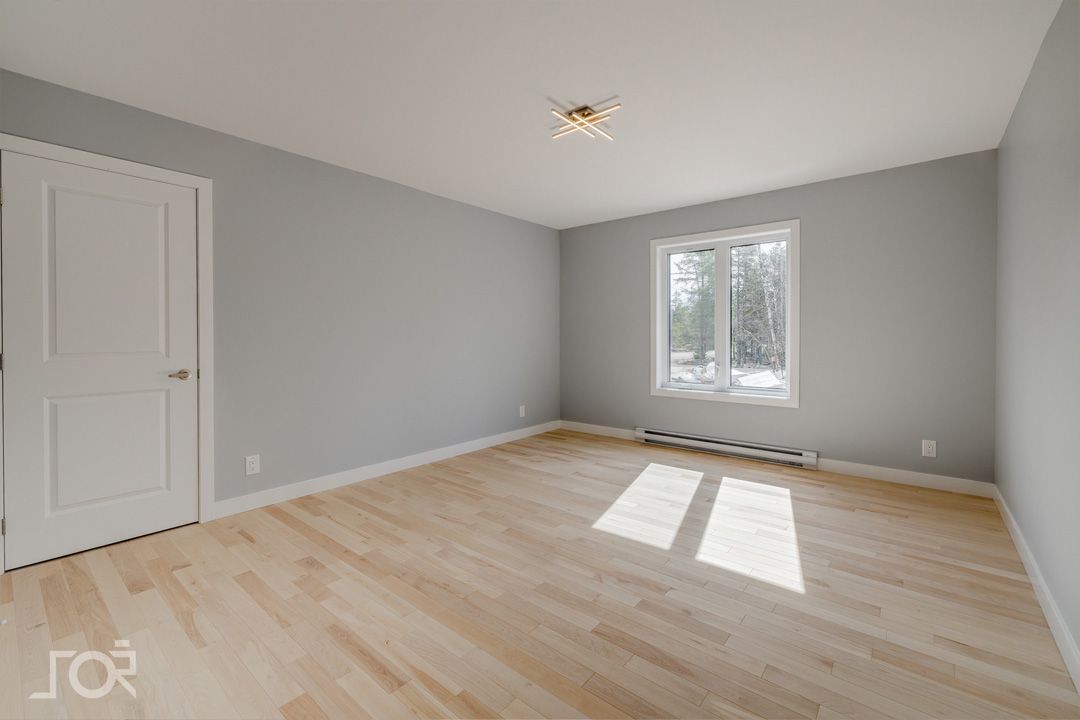 Une grande pièce vide avec du parquet et des murs gris.