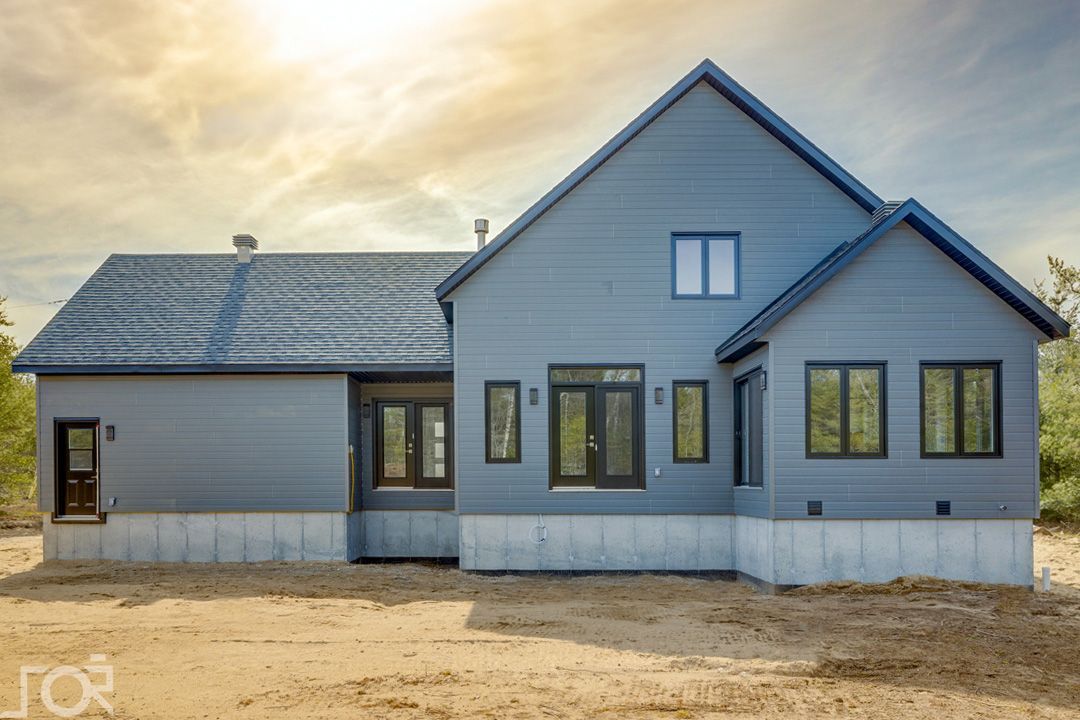 Une grande maison avec beaucoup de fenêtres est située au sommet d'un champ de terre.
