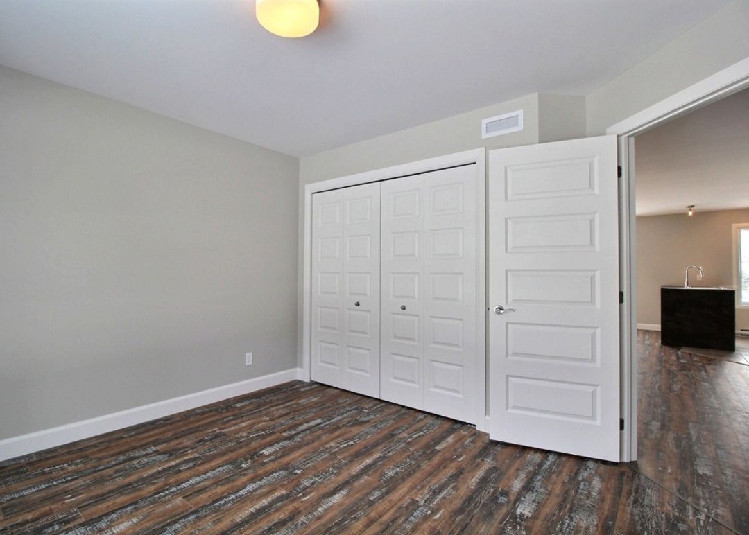 Une chambre vide avec du parquet et des portes de placard blanches.