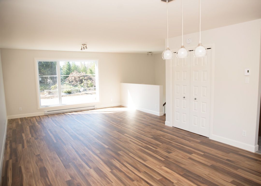 Un salon vide avec du parquet et des murs blancs.