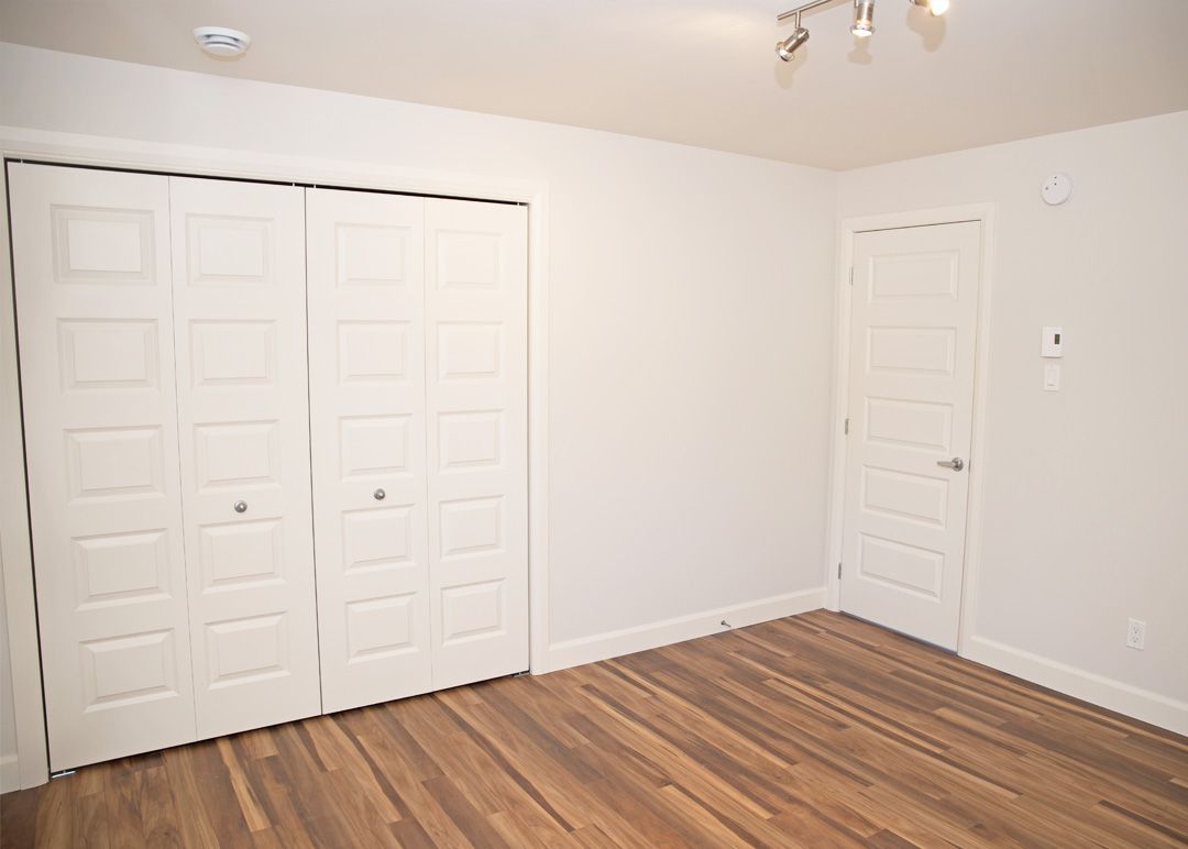 Une chambre vide avec du parquet et des murs blancs.