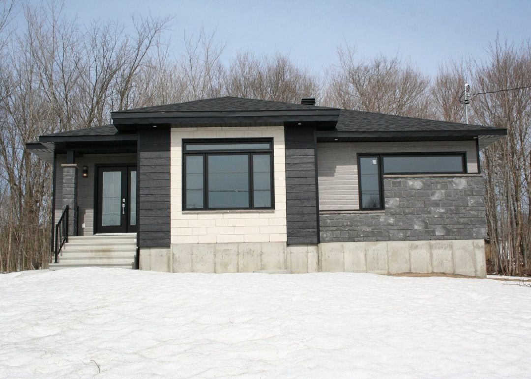 Une maison au toit noir se trouve au milieu d'un champ enneigé