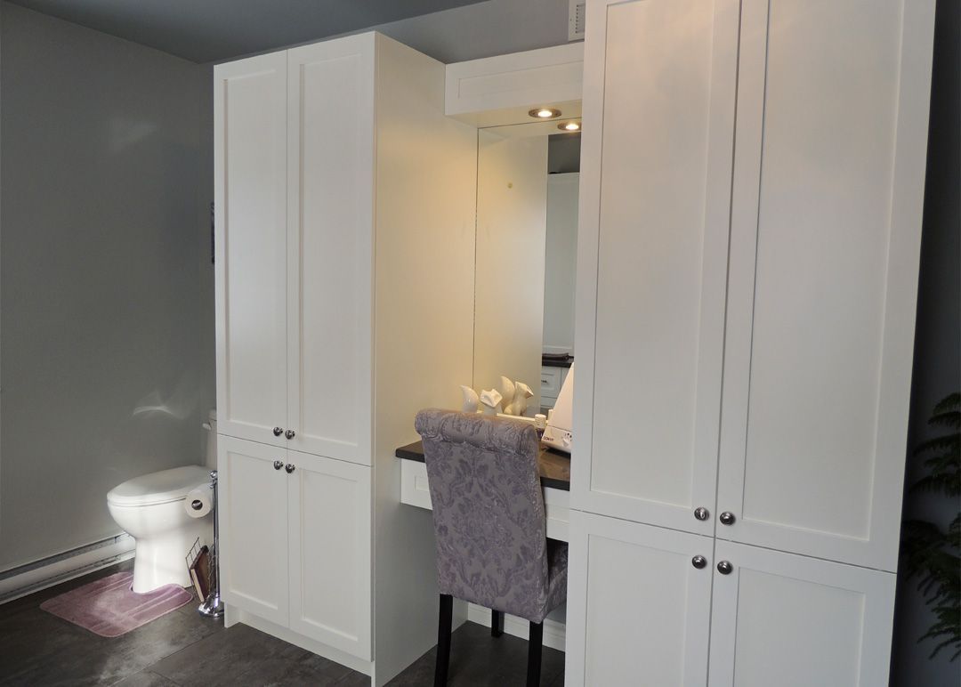 Une salle de bain avec des armoires blanches, des toilettes, un bureau et une chaise.