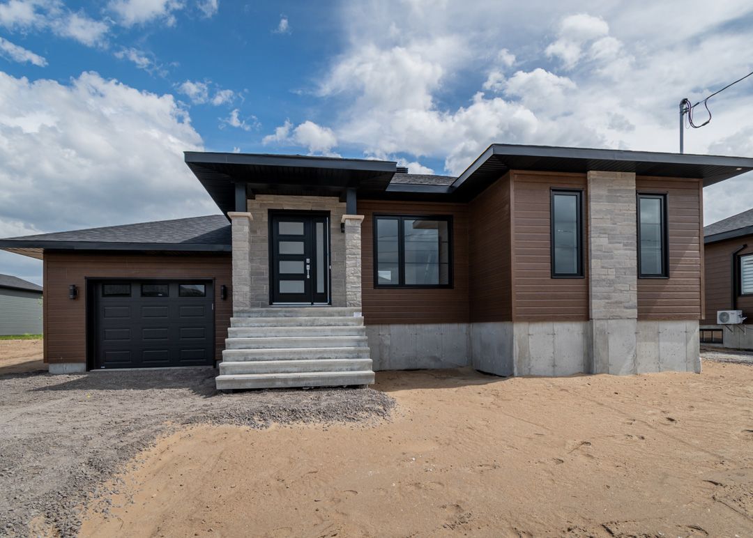 Une maison avec beaucoup de fenêtres et un garage est située au sommet d'un champ de terre.