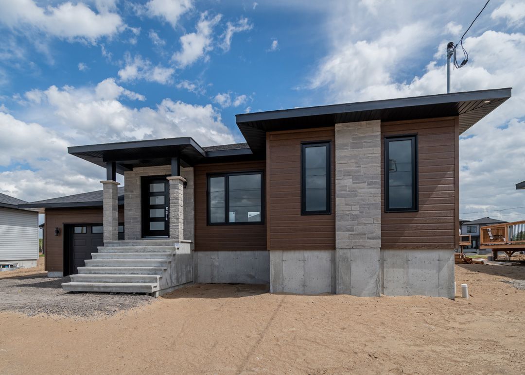 Une maison moderne avec beaucoup de fenêtres est située au sommet d'un champ de terre.