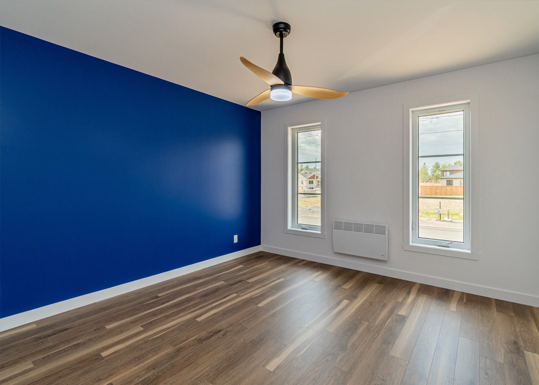 Une pièce vide avec un ventilateur de plafond et deux fenêtres.