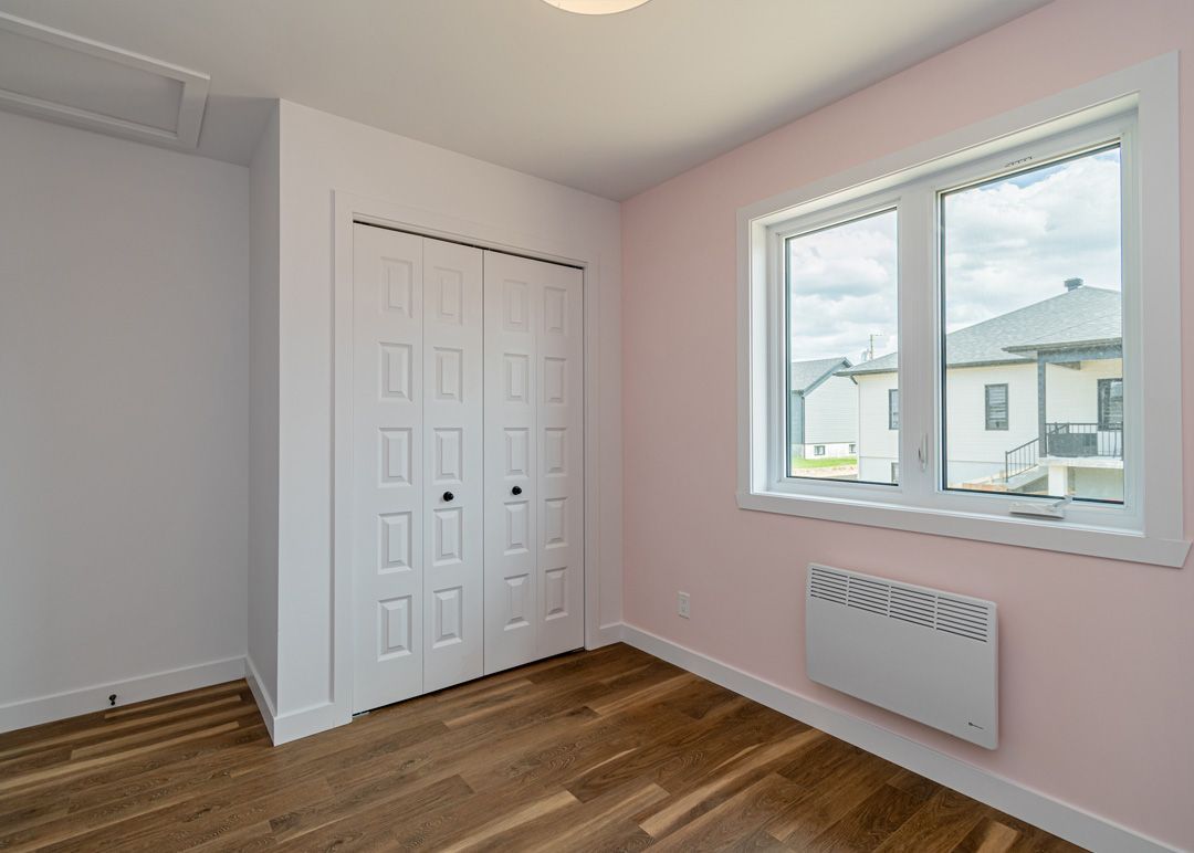 Une chambre vide avec des murs roses et une grande fenêtre.