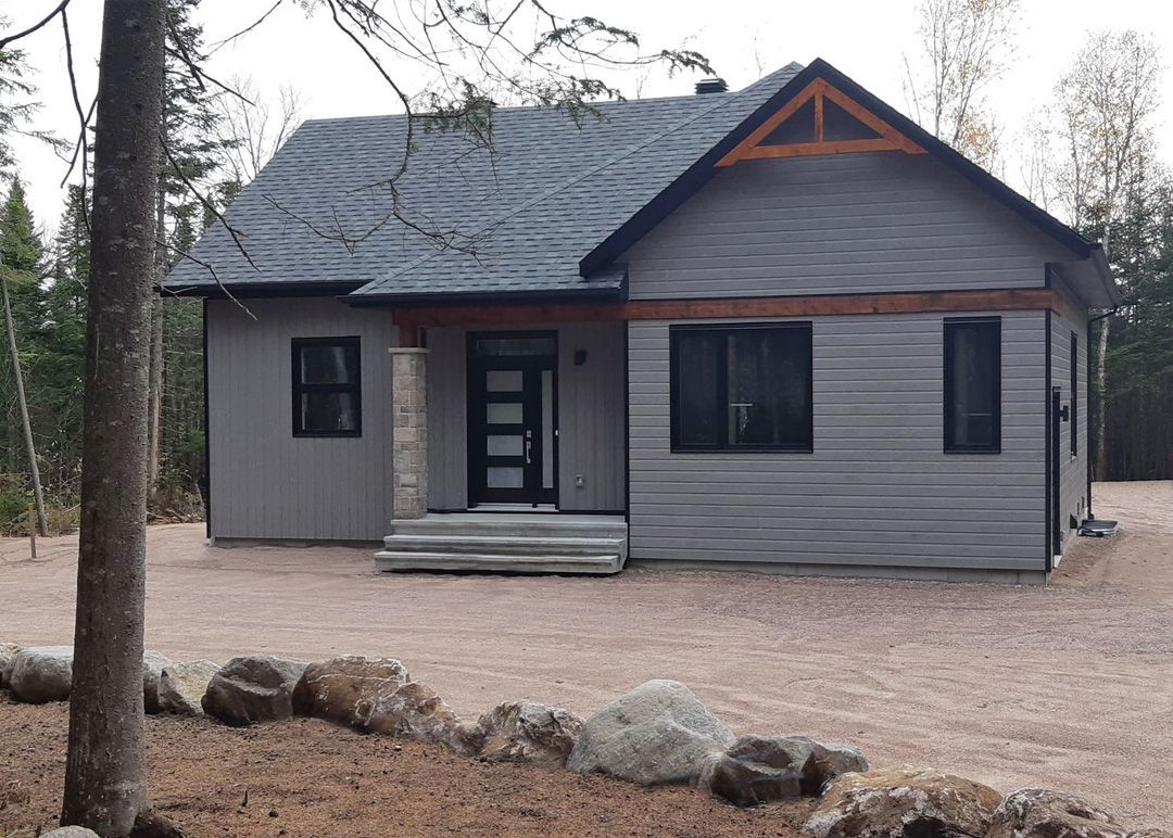 Une petite maison est assise au sommet d'un champ de terre au milieu d'une forêt.