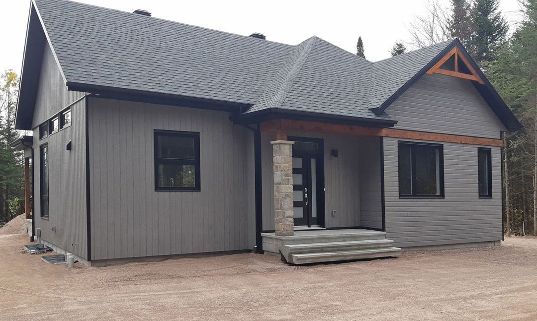 Une petite maison au toit gris est assise au sommet d'un champ de terre.