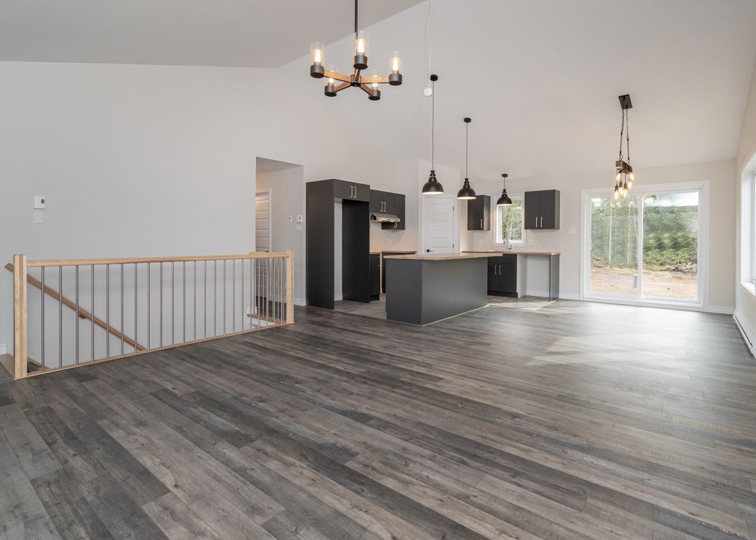 Une grande pièce vide avec du parquet et une cuisine en arrière-plan.