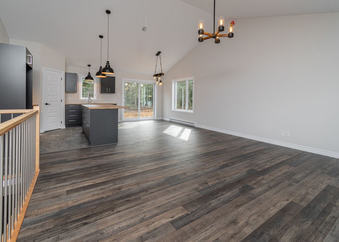 Un salon vide avec du parquet et une cuisine en arrière-plan.