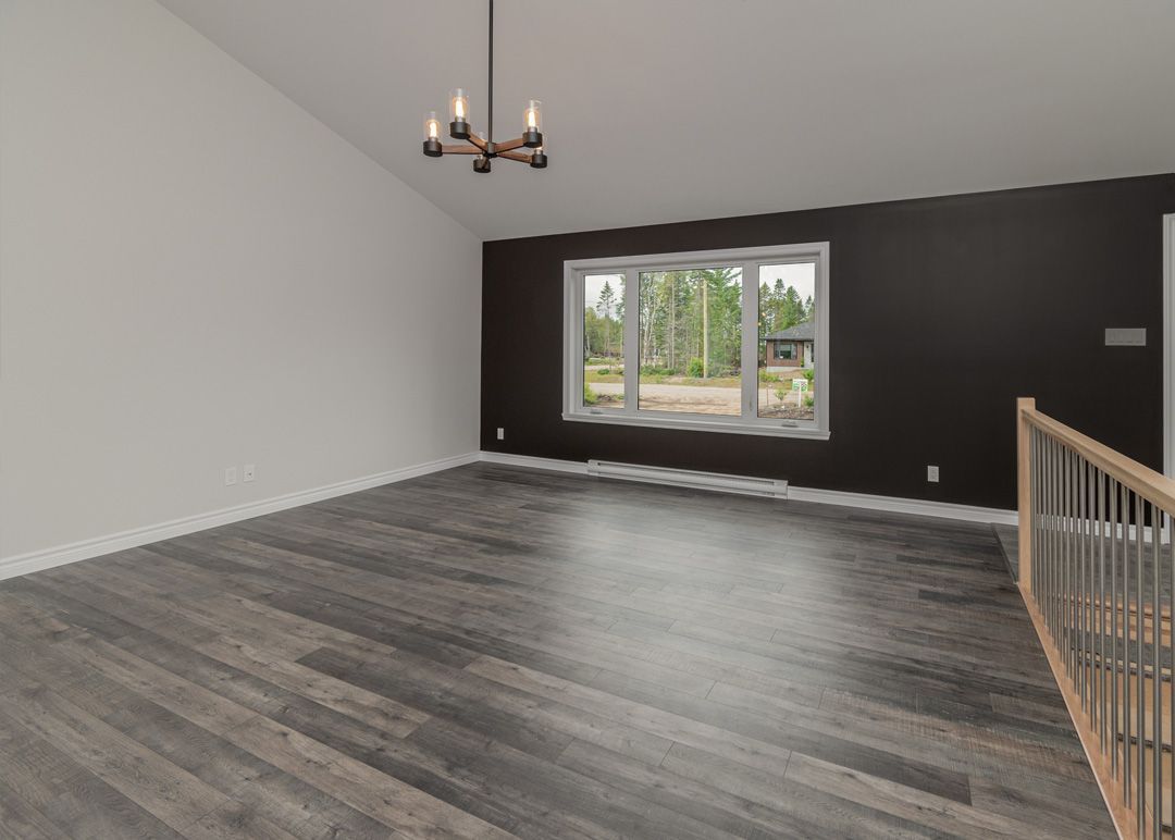 Un salon vide avec du parquet et un lustre suspendu au plafond.