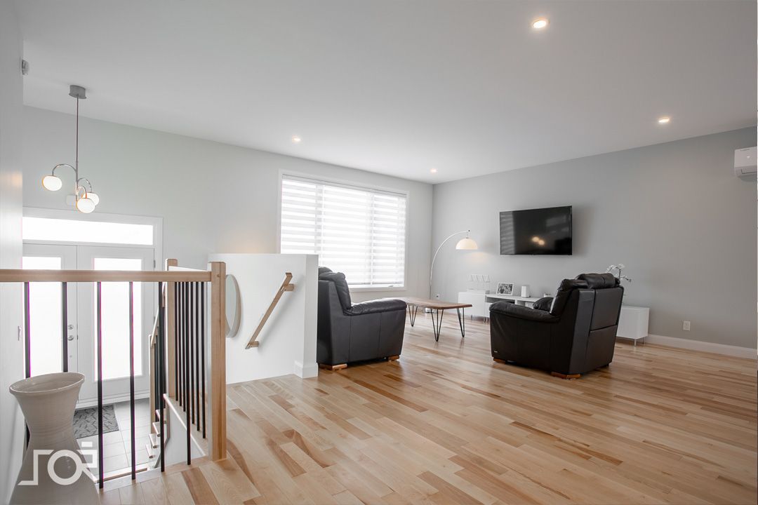 Un salon avec parquet et une télévision au mur.