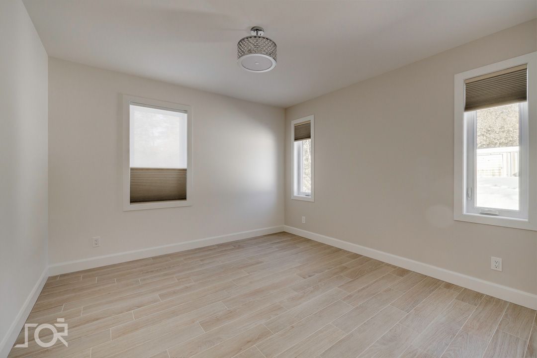 Une chambre vide avec deux fenêtres et un plafonnier.