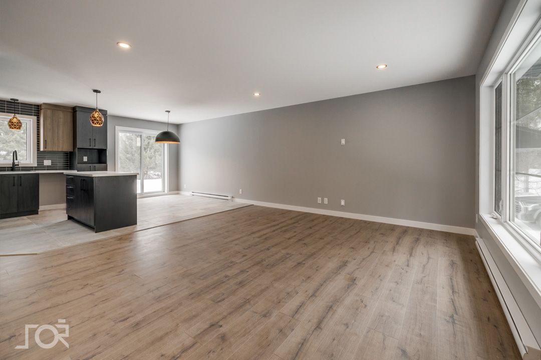 Un salon vide avec du parquet et une cuisine en arrière-plan.