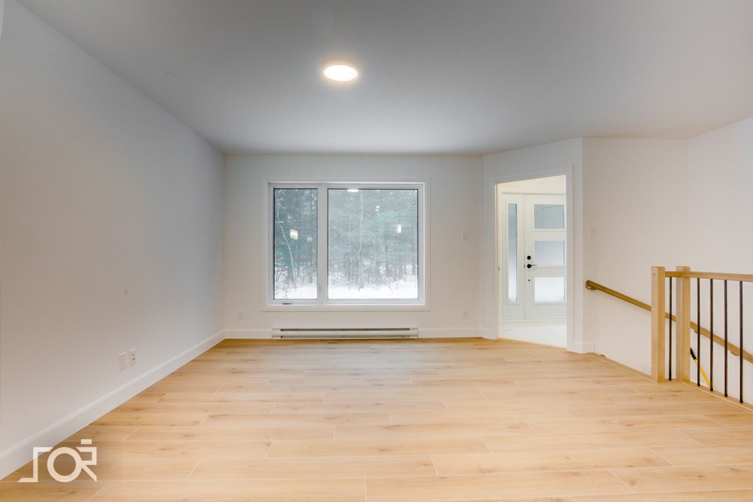 Un salon vide avec du parquet et une grande fenêtre.