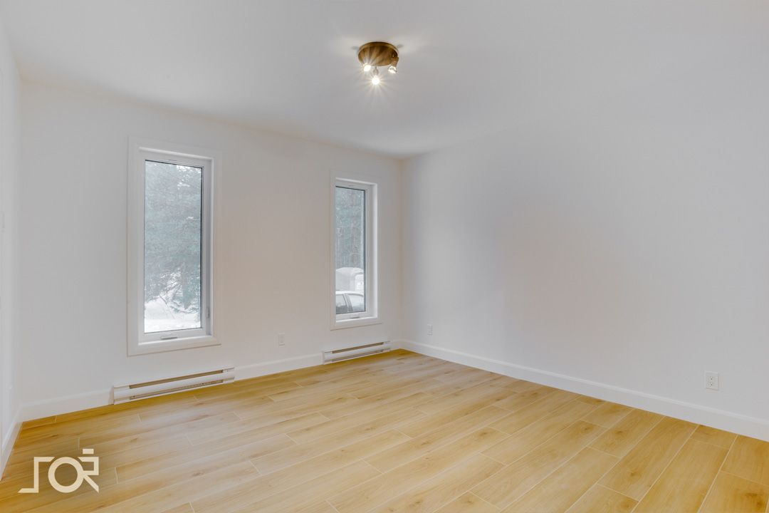 Une pièce vide avec du parquet et deux fenêtres.