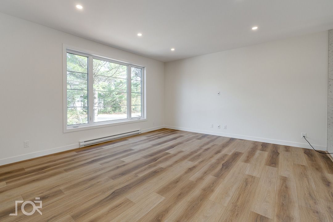 Un salon vide avec parquet et grandes fenêtres.