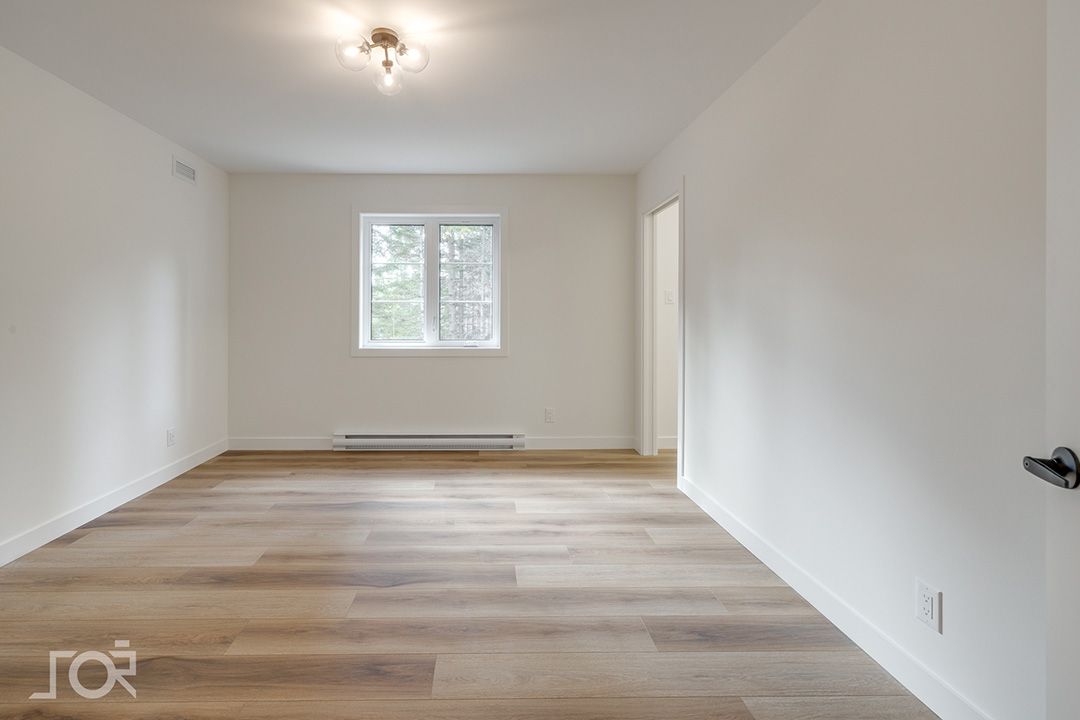 Un salon vide avec du parquet et des murs blancs.