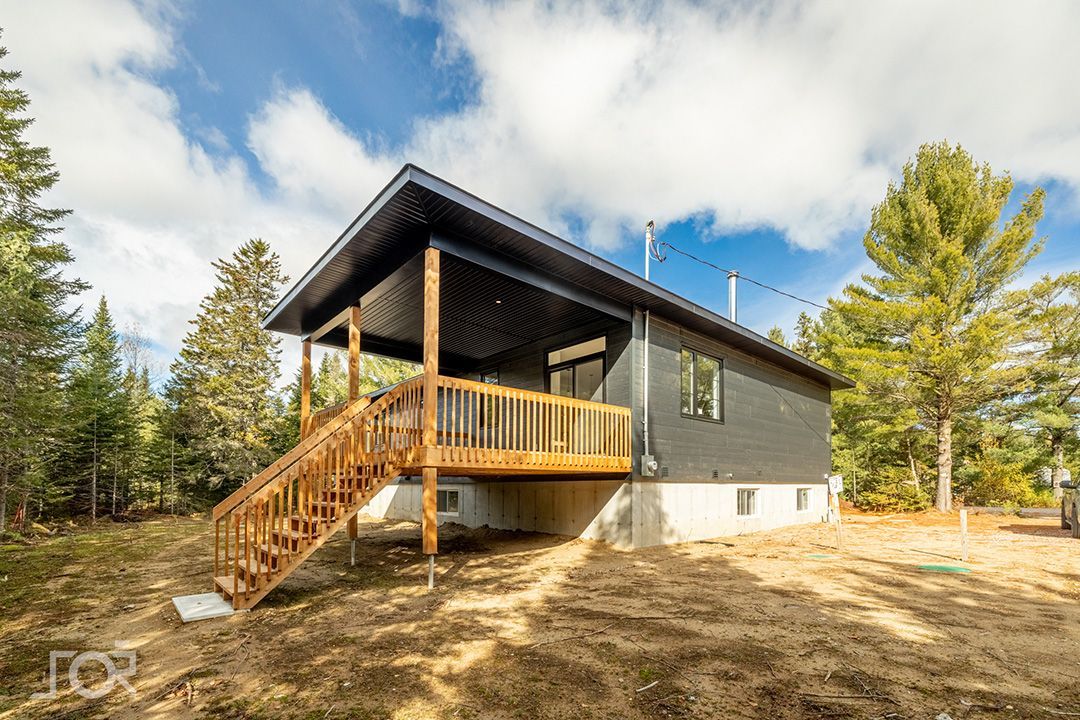 Une petite maison avec une terrasse en bois et des escaliers au milieu d'une forêt.
