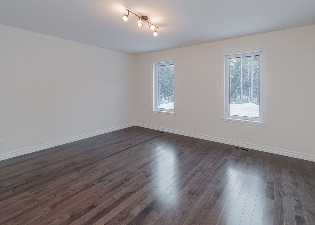 Une pièce vide avec du parquet et deux fenêtres.