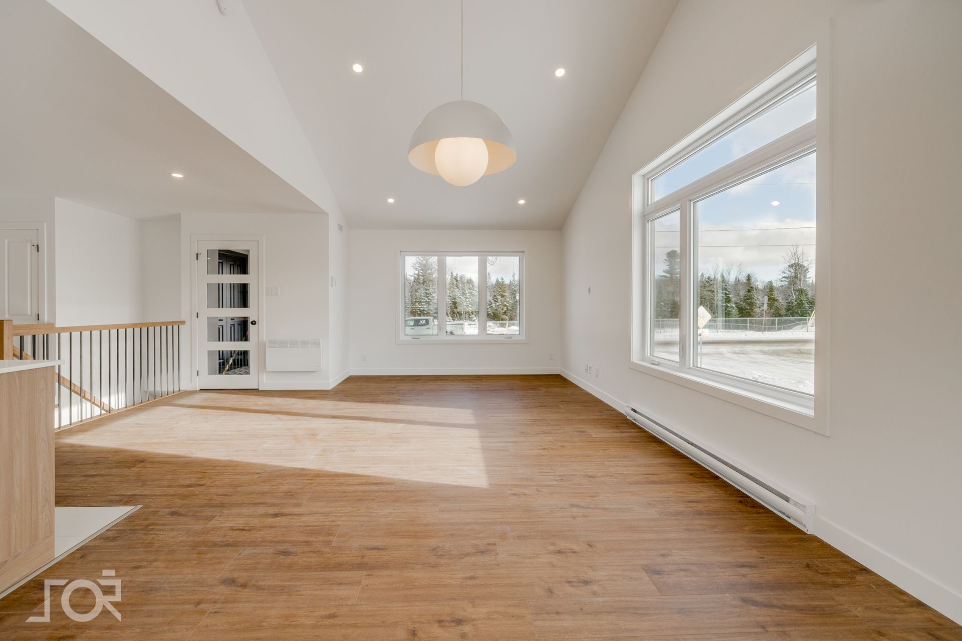 Salon moderne vide avec parquet, murs blancs et grandes fenêtres.