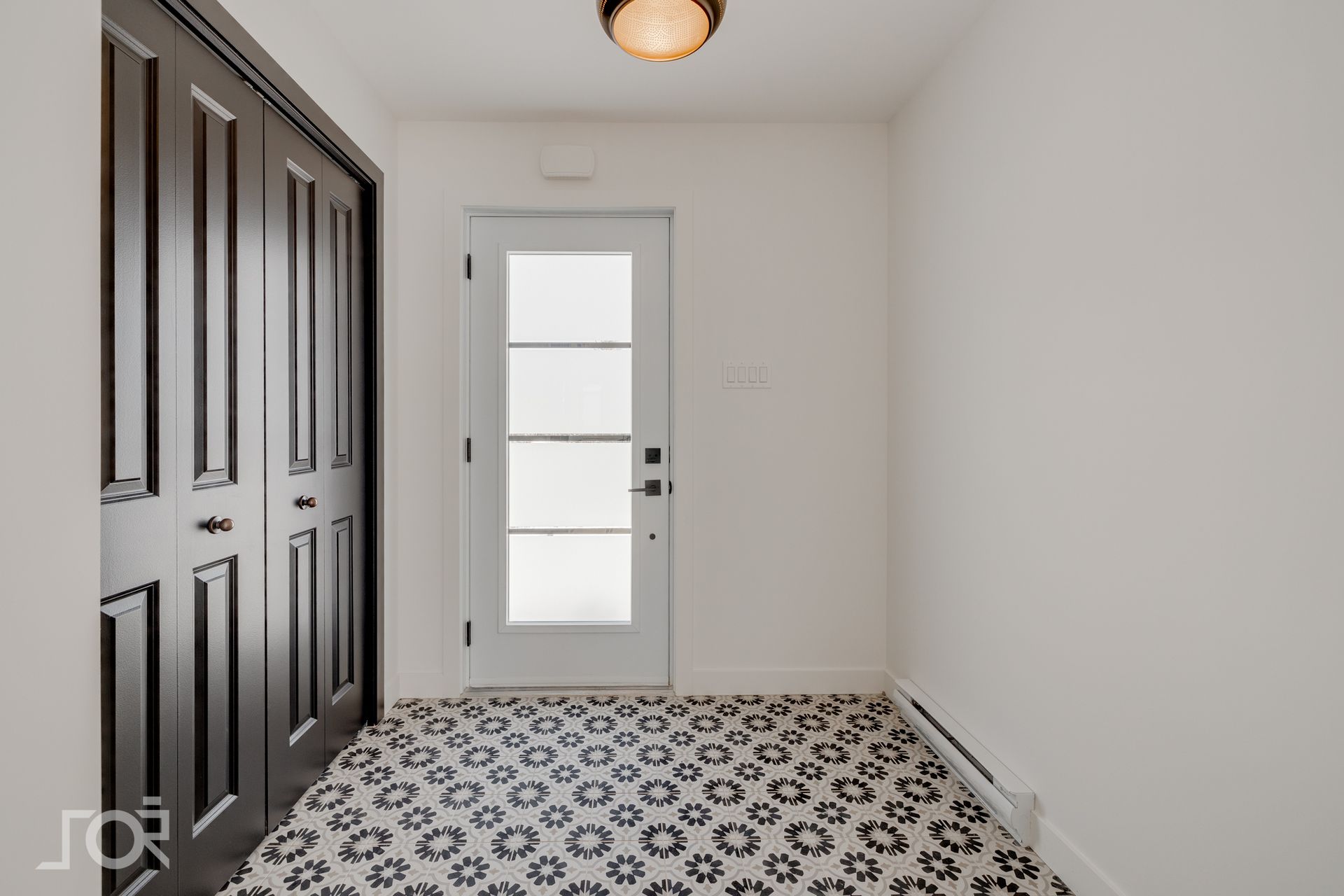 Entrée avec sol carrelé de carreaux noirs à motifs, portes de placard noires, murs blancs et porte blanche à panneaux de verre.