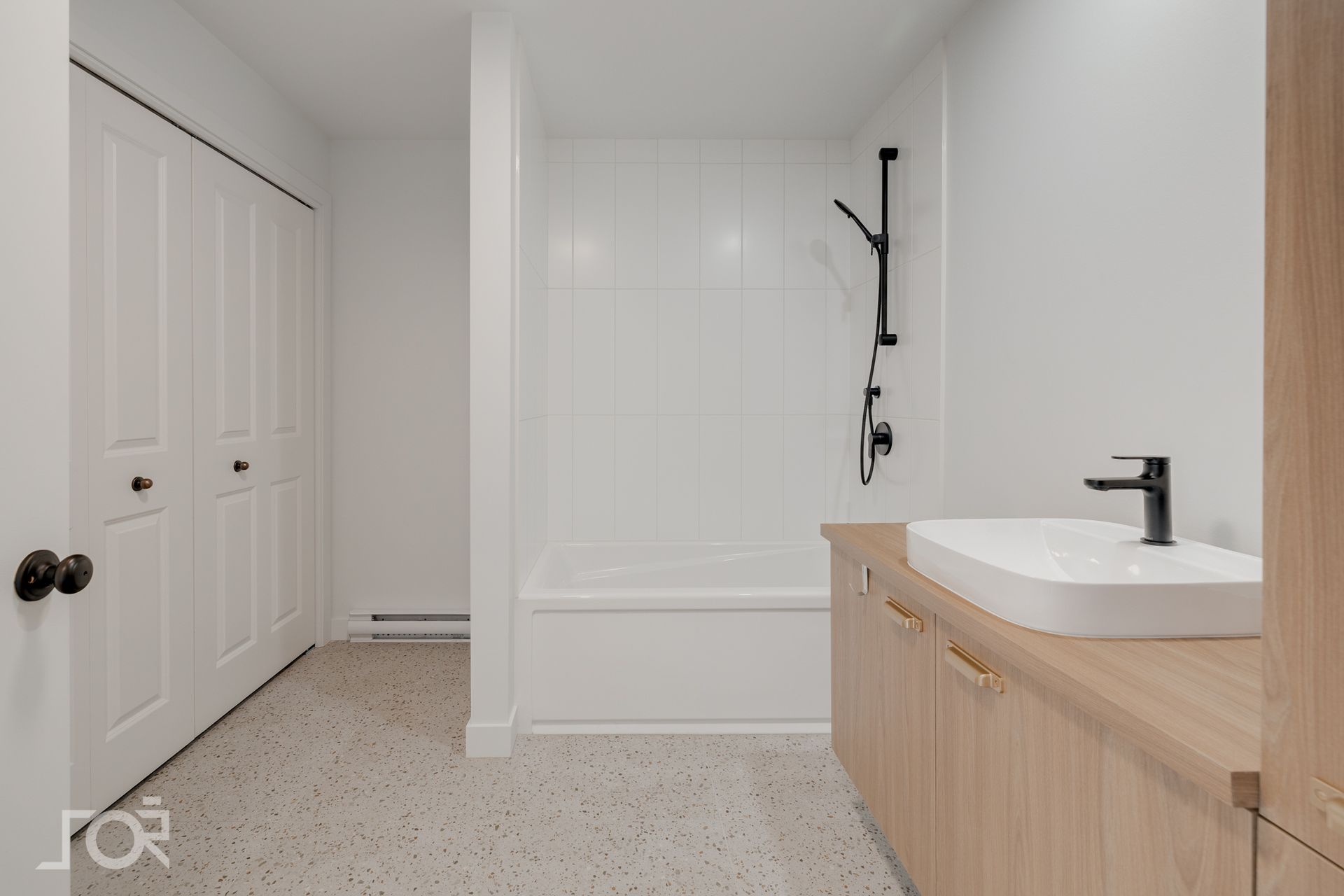Salle de bains avec murs blancs, douche/baignoire, meuble-lavabo en bois clair avec lavabo et robinetterie noire.