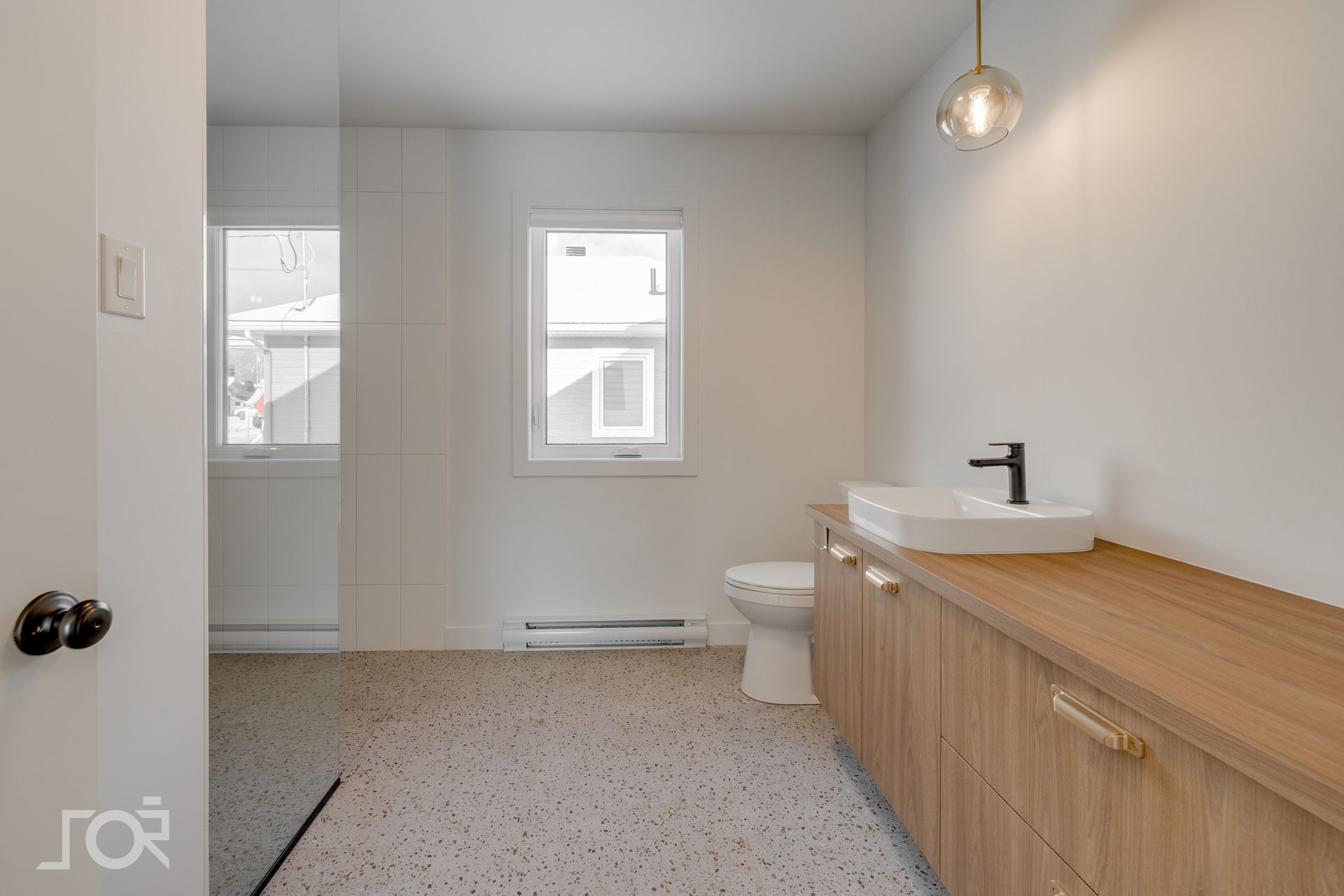 Salle de bains avec meuble-lavabo en bois, vasque, toilettes blanches et sol moucheté.