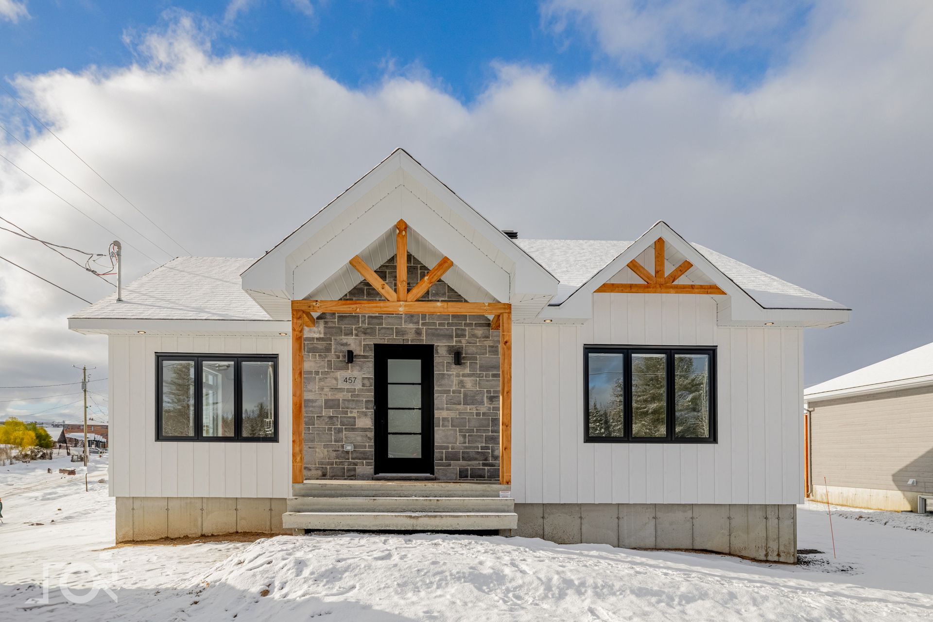 Maison blanche à la façade en pierre, avec des éléments en bois, et un environnement enneigé sous un ciel bleu.
