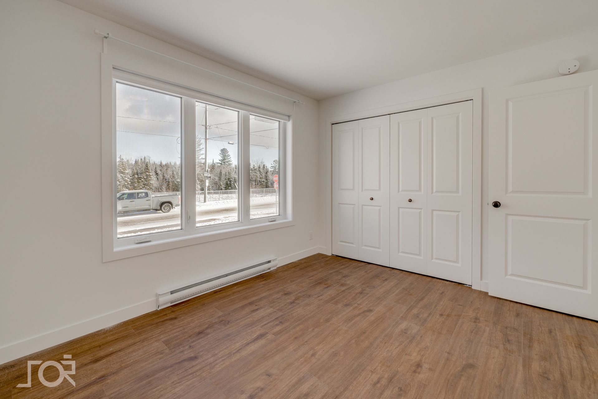 Pièce vide avec parquet, murs blancs, grande fenêtre et placard.